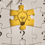 An image of a lightbulb on a yellow jigsaw piece, surrounded by white jigsaw pieces with question marks
