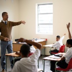 A teacher responds to a handful of students who have their arms up asking questions. 
