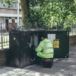 An image of a man kneeling down fixing a street-level power box