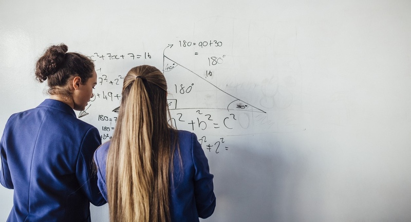 Two girls solving a math problem on a whiteboard