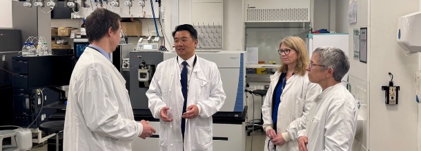 Four individuals in lab coats are stood in a lab in discussion. 