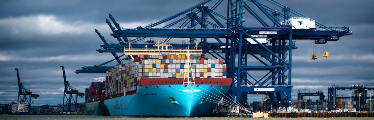 An image of a cargo ship docked underneath three blue cranes. 