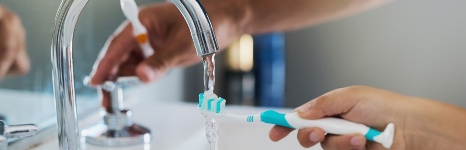 toothbrush being rinsed by water coming from a tap