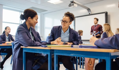 A secondary school class, with two students in the foreground smiling at one another.