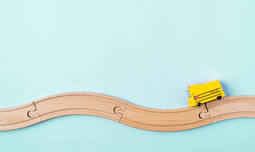 Wooden road puzzle with yellow toy school bus on blue background