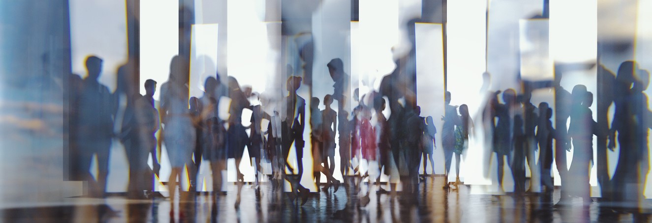 Blurred image of many people in an enclosed work environment.